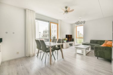 Çağdaş dairenin geniş odasındaki dinlenme odası ve mutfağın yakınındaki sandalyeli ve çiçekli masa.