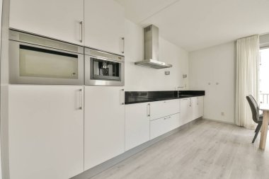 Çağdaş dairenin geniş odasındaki dinlenme odası ve mutfağın yakınındaki sandalyeli ve çiçekli masa.