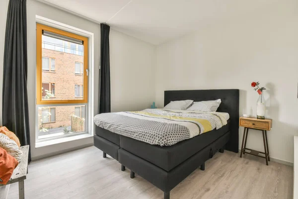 Parlayan lambanın yanında rahat bir yatak ve küçük pencereli çağdaş yatak odasında çerçeveli resimler.