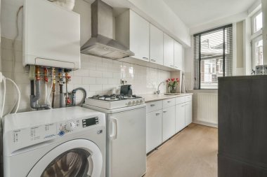 Çağdaş mutfaktaki beyaz dolaplarla tezgahların üzerine çeşitli mutfak malzemeleri ve aletler yerleştirilmiş.