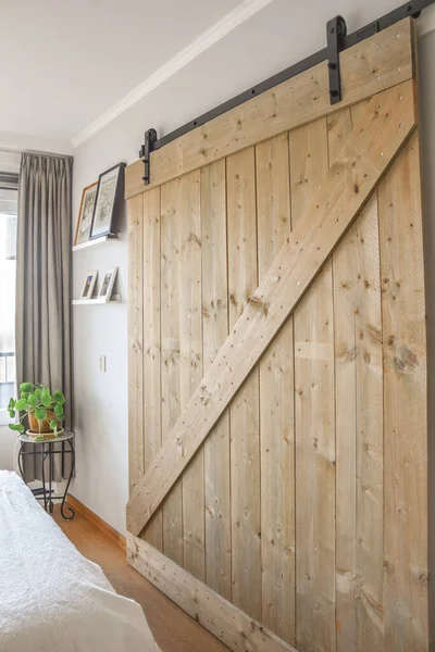 Comfortable bed with duvet and pillows located near chair and wall with framed painting against wardrobe in illuminated bedroom