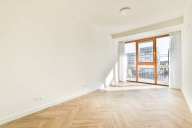 Pencereleri ve ahşap parke zemini olan boş beyaz mutfağın içi.