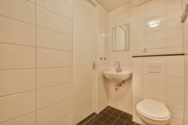 Modern sifon tuvaleti ve seramik lavabo aynanın yanındaki beyaz fayanslı duvarlara ve evdeki küçük tuvaletteki havluya monte edildi.