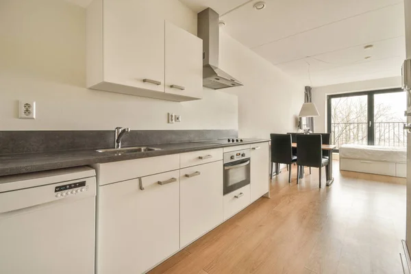 Interior of light kitchen with modern cupboards and appliances located near dining room in modern flat at daytime