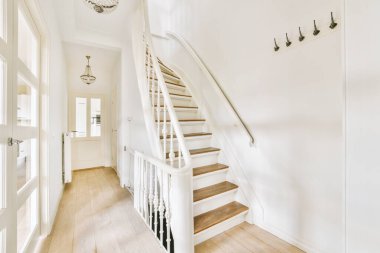 Minimalist iç tasarımı olan modern lüks dairenin ikinci katına çıkan ahşap merdivenli beyaz koridor.