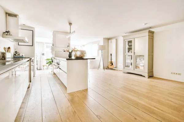 Modern minimalist style interior design of studio apartment with open white kitchen and dining zone with table and chairs illuminated by loft style lamp