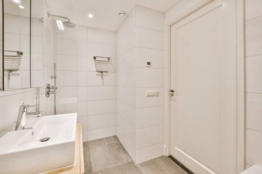 Aynalı lavabo ve temiz küvet modern banyoda cam kapılı ve beyaz fayanslı duvarları olan duş kutusunun yanında.