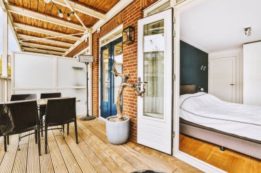 Dar tuğlalı balkon, metal parmaklıklar, tahta sandalye ve kapı.