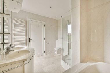 Tiled shower cabin with glass door located near sink and toilet in light restroom in contemporary apartment