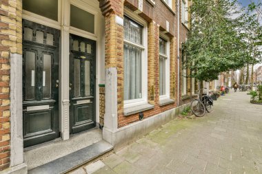 Levhalı, kaldırımlı ve ahşap kapılı bir binanın ön manzarası daireye çıkıyor.