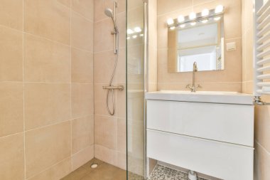 Modern banyoda aynalı lavabo ve cam kapılı duş kutusu ve beyaz fayanslı duvarlar.