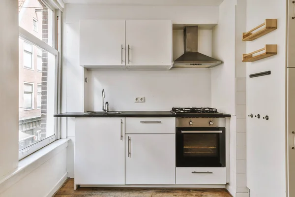 Well organized small home kitchen interior with sink under window and light furniture with stove and fridge in urban apartment