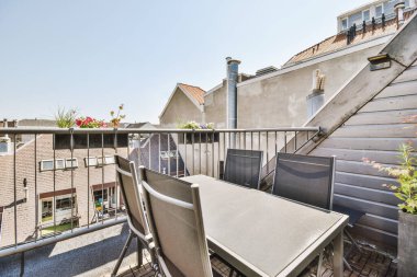 Parlak tuğla balkon, metal parmaklıklar, tahta sandalye ve kapı.