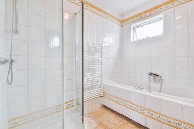 Aynalı lavabo ve temiz küvet modern banyoda cam kapılı ve beyaz fayanslı duvarları olan duş kutusunun yanında.