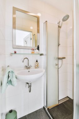 Modern banyoda aynalı lavabo ve cam kapılı duş kutusu ve beyaz fayanslı duvarlar.