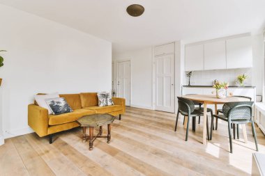 Günümüz minimalist tasarımı. Hafif stüdyo dairesinin ahşap masası ve oturma odası ile beyaz duvarları ve parke zemini arasında yemek masası ve sandalyeleri var.