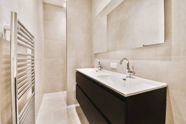 Evdeki çağdaş tuvaletteki aynanın altındaki duvarda musluk ve sıvı sabun asılı.