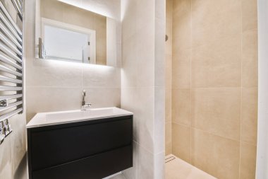 Evdeki çağdaş tuvaletteki aynanın altındaki duvarda musluk ve sıvı sabun asılı.