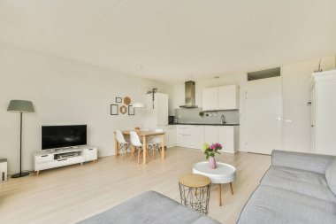 Çağdaş dairenin geniş odasındaki dinlenme odası ve mutfağın yakınındaki sandalyeli ve çiçekli masa.