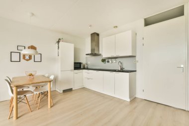 Çağdaş dairenin geniş odasındaki dinlenme odası ve mutfağın yakınındaki sandalyeli ve çiçekli masa.