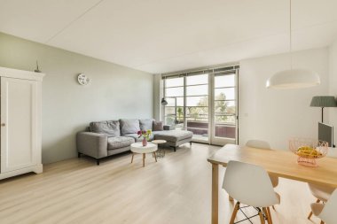 Çağdaş dairenin geniş odasındaki dinlenme odası ve mutfağın yakınındaki sandalyeli ve çiçekli masa.