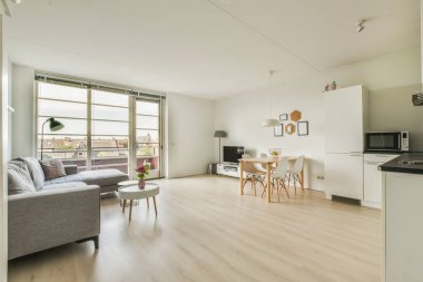 Çağdaş dairenin geniş odasındaki dinlenme odası ve mutfağın yakınındaki sandalyeli ve çiçekli masa.