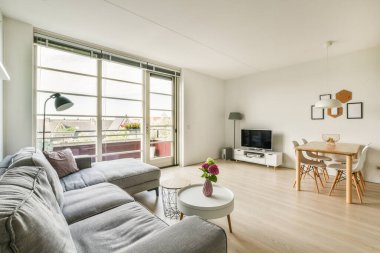 Çağdaş dairenin geniş odasındaki dinlenme odası ve mutfağın yakınındaki sandalyeli ve çiçekli masa.