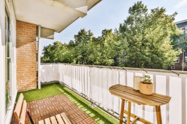 Dar tuğlalı balkon, metal parmaklıklar, tahta sandalye ve kapı.