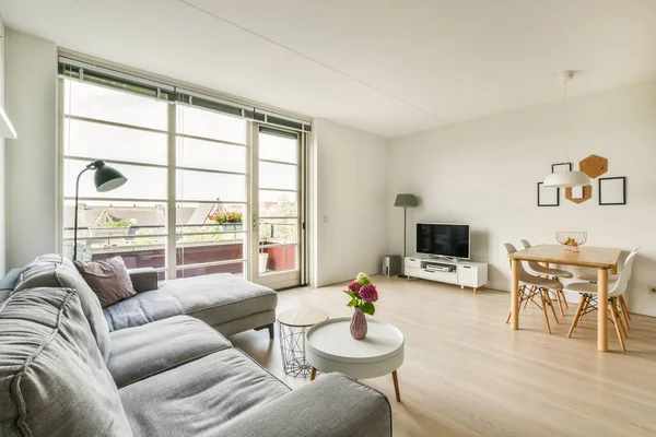 Çağdaş dairenin geniş odasındaki dinlenme odası ve mutfağın yakınındaki sandalyeli ve çiçekli masa.