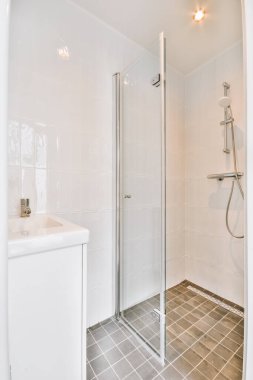 Modern banyoda aynalı lavabo ve cam kapılı duş kutusu ve beyaz fayanslı duvarlar.