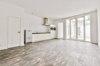 Pencereleri ve ahşap parke zemini olan boş beyaz mutfağın içi.