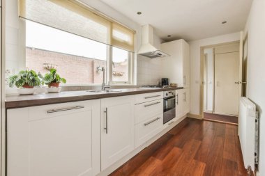 Gündüz vakti modern bir dairede yemek odasının yakınında modern dolaplar ve aletlerle donatılmış aydınlık mutfağın içi.