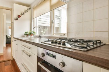 Gündüz vakti modern bir dairede yemek odasının yakınında modern dolaplar ve aletlerle donatılmış aydınlık mutfağın içi.