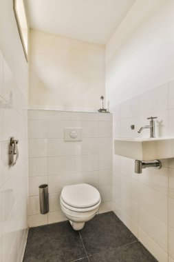 Duvara asılmış tuvalet ve köşedeki bej fayanslı lavabo.