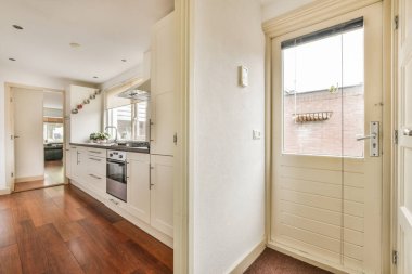 Gündüz vakti modern bir dairede yemek odasının yakınında modern dolaplar ve aletlerle donatılmış aydınlık mutfağın içi.