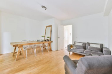 Sandalyeleri ve vazosu olan eski püskü ahşap masa modern apartmanda dekorasyonlu aydınlık duvarlara karşı rahat kanepenin yanında.