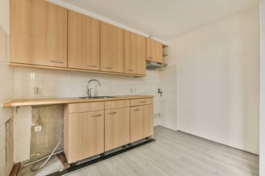 Pencereleri ve ahşap parke zemini olan boş beyaz mutfağın içi.