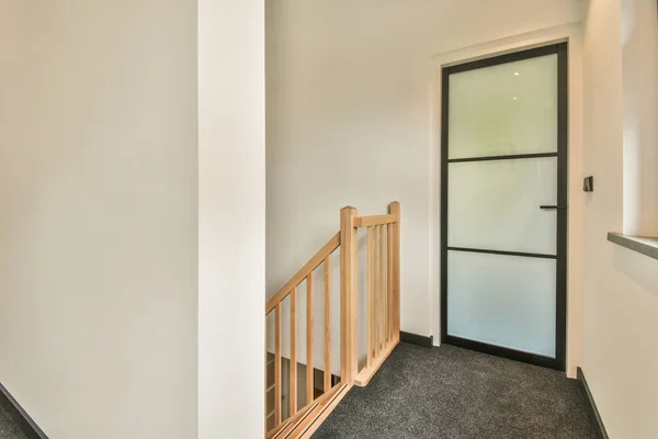 Light narrow hallway with door in two level apartment with minimalist wooden staircase