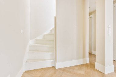 Minimalist iç tasarımı olan modern lüks dairenin ikinci katına çıkan ahşap merdivenli beyaz koridor.