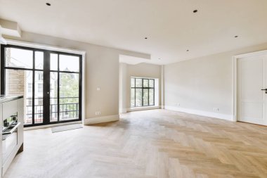 Pencereleri ve ahşap parke zemini olan boş beyaz mutfağın içi.