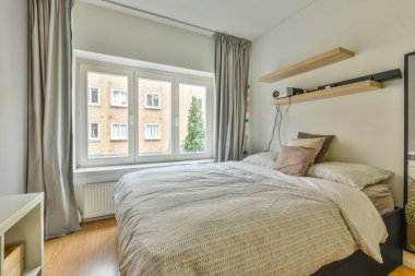 Comfortable bed with white bedclothes and bedside table placed near window in light bedroom at home