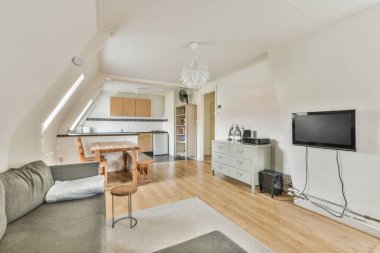 Table with chairs and flowers on the windowsill near lounge area and kitchen in spacious attic room of contemporary apartment