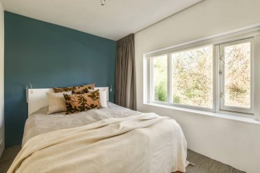 Comfortable bed with white bedclothes near window in light bedroom at home