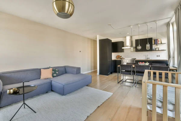 Table with chairs and sofa near lounge area ,kitchen and washing machine in spacious room of contemporary apartment