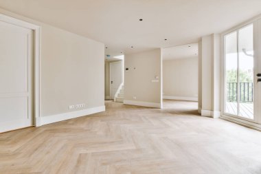 Pencereleri ve ahşap parke zemini olan boş beyaz mutfağın içi.