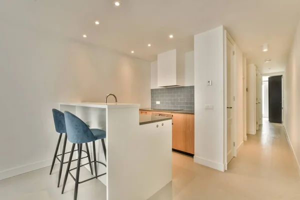 Contemporary counters and stools located under stylish exhaust hood in spacious light kitchen at home