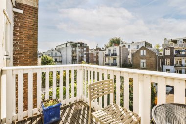 Dar tuğlalı balkon, metal parmaklıklar, tahta sandalye ve kapı.