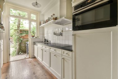 İyi organize edilmiş küçük bir ev mutfağı pencerenin altında lavabo, sobalı hafif mobilyalar ve kentsel apartmanda buzdolabı var.