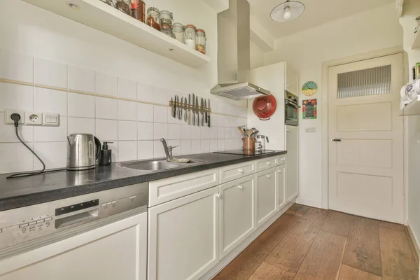 Well organized small home kitchen interior with sink under window and light furniture with stove and fridge in urban apartment