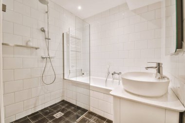 Aynalı lavabo ve temiz küvet modern banyoda cam kapılı ve beyaz fayanslı duvarları olan duş kutusunun yanında.